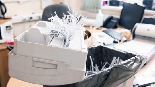 Small office shredder on desk with documents ready for secure disposal